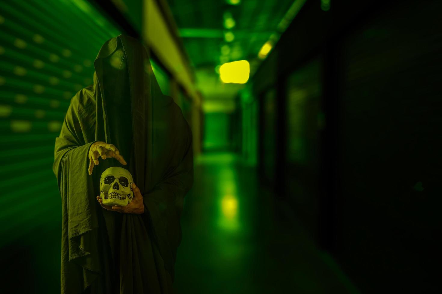 Horror scene of scary mysterious black man holding a skull in his hand at a creepy old building corridor photo