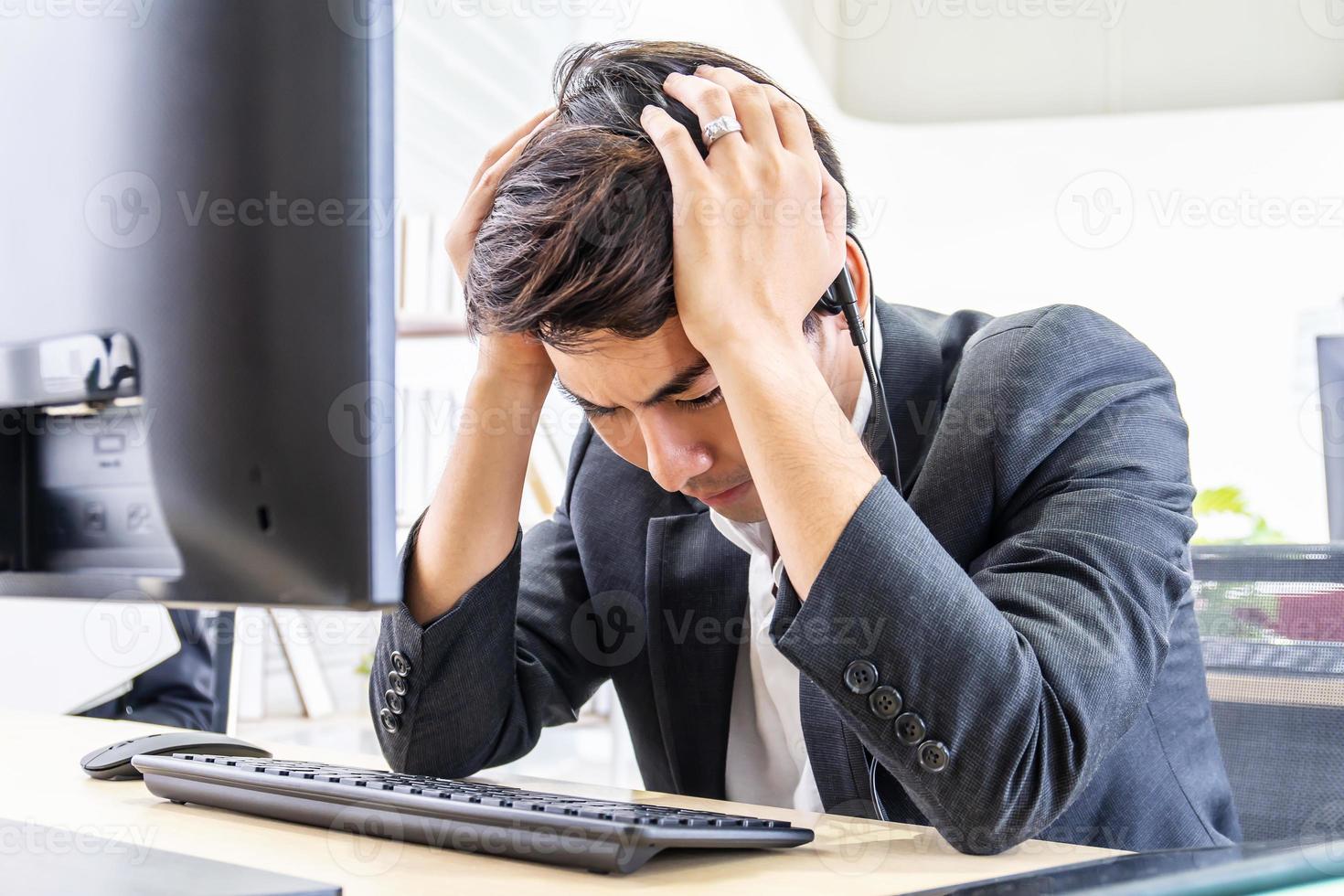 Young asian operator man wearing call center headset Feeling stress  and headache from work in the office photo