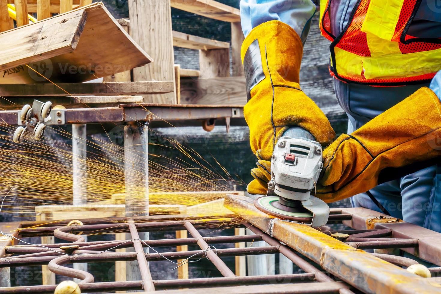 Young man welder in a working blue overall and working gloves grinds a metal object with a angle grinder in the garage, bright sparks fly to the sides photo