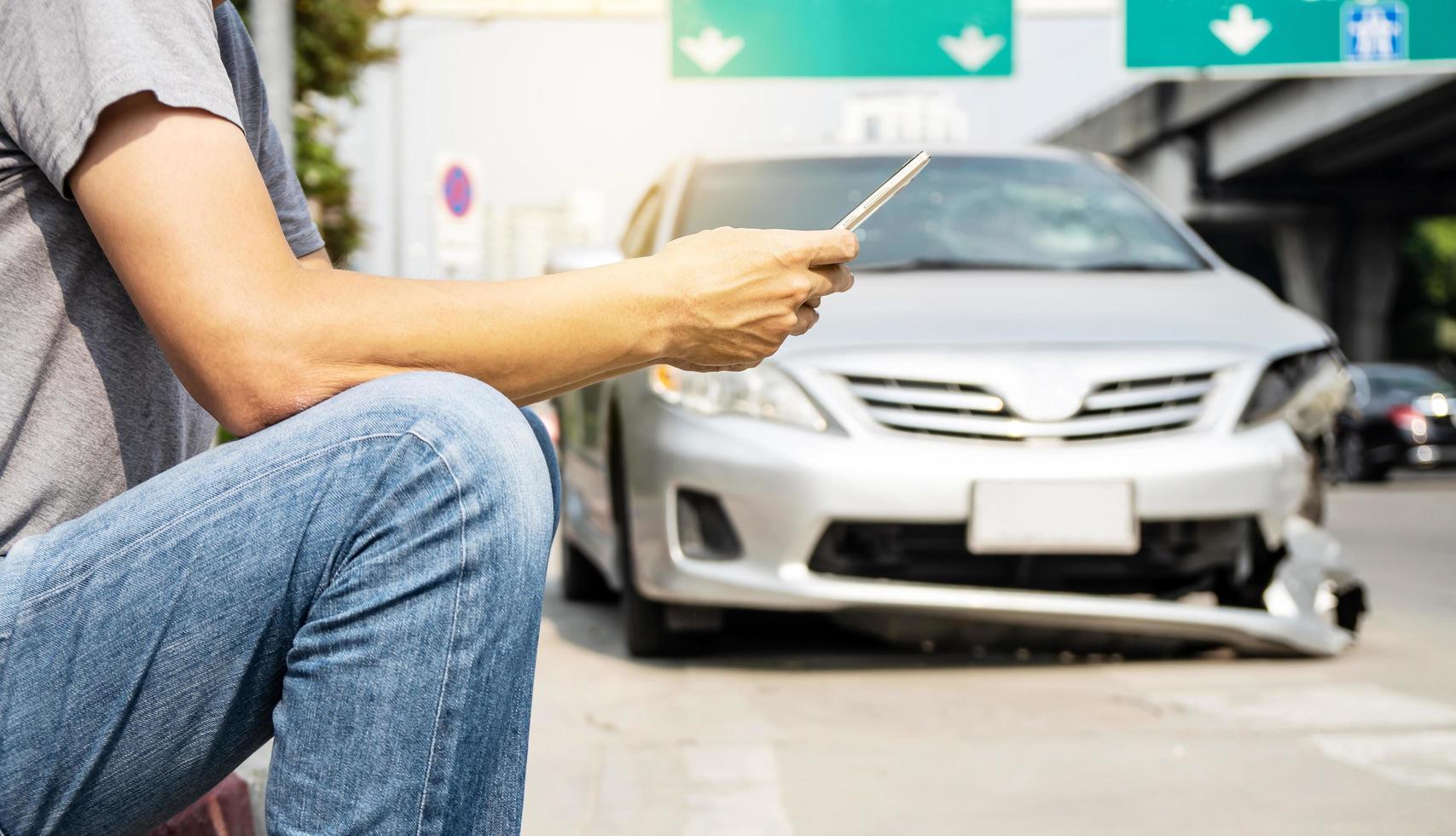 hombre que usa la ayuda de un teléfono inteligente para llamar a la compañía de seguros o al servicio de recuperación en la carretera después de un accidente de tráfico foto