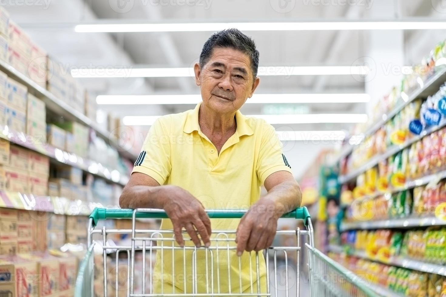 Asian senior man shopping trolley choosing other products in supermarket photo