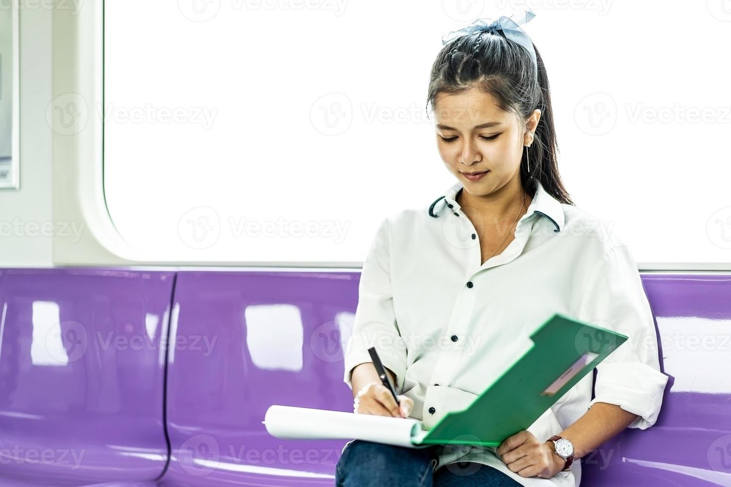 Beautiful asian woman working urgently writing on sheet of paper in a clipboard with pen at the electric train in the morning photo