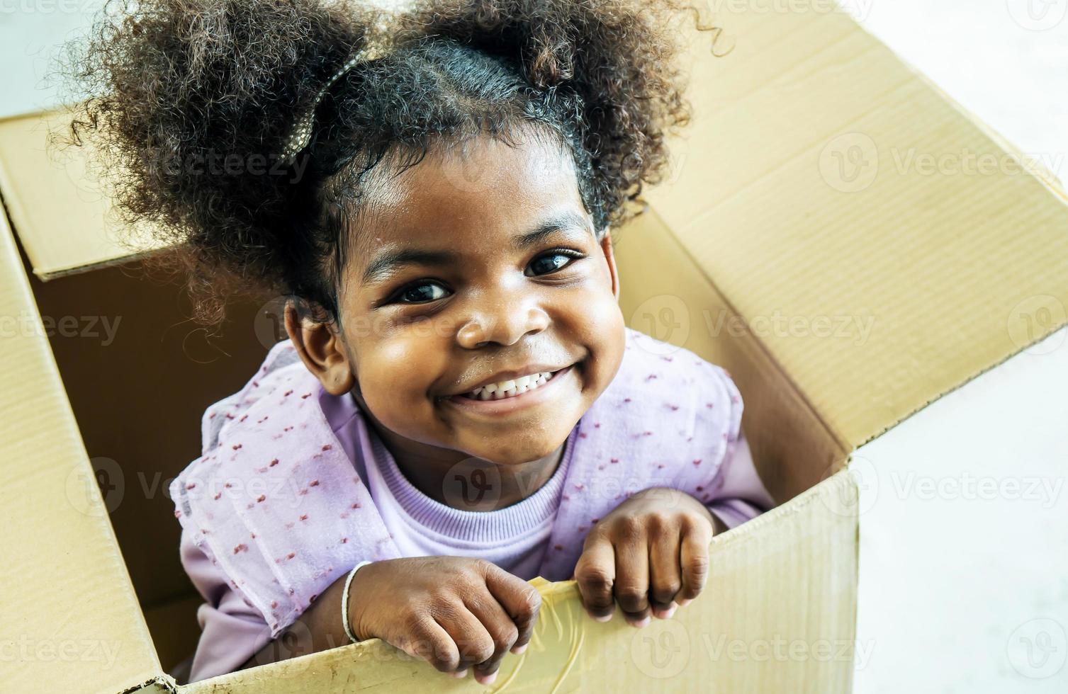 Happy cute active little african american kids girl play riding in cardboard boxes feel excited to move in new house, playful overjoyed black sister have fun photo