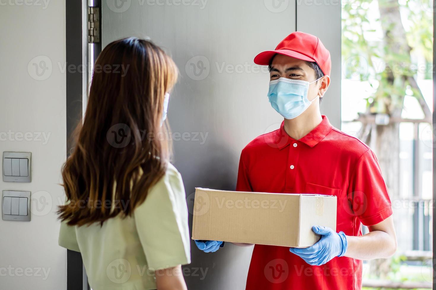 Delivery man in red uniform holdinging parcel boxes to a woman customer - courier service concept photo