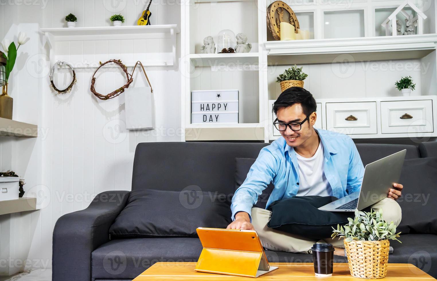 Smart Asian businessman in casual clothing sitting on a sofa in the house is working on computer laptop and tablet , SME start up concept, work from home photo