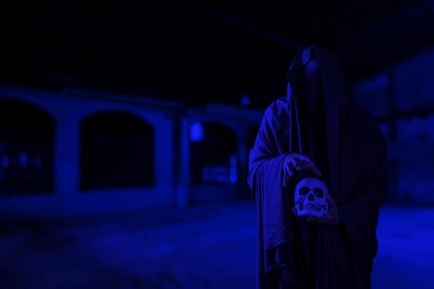 Horror scene of scary mysterious black man holding a skull in his hand at a creepy old building corridor photo