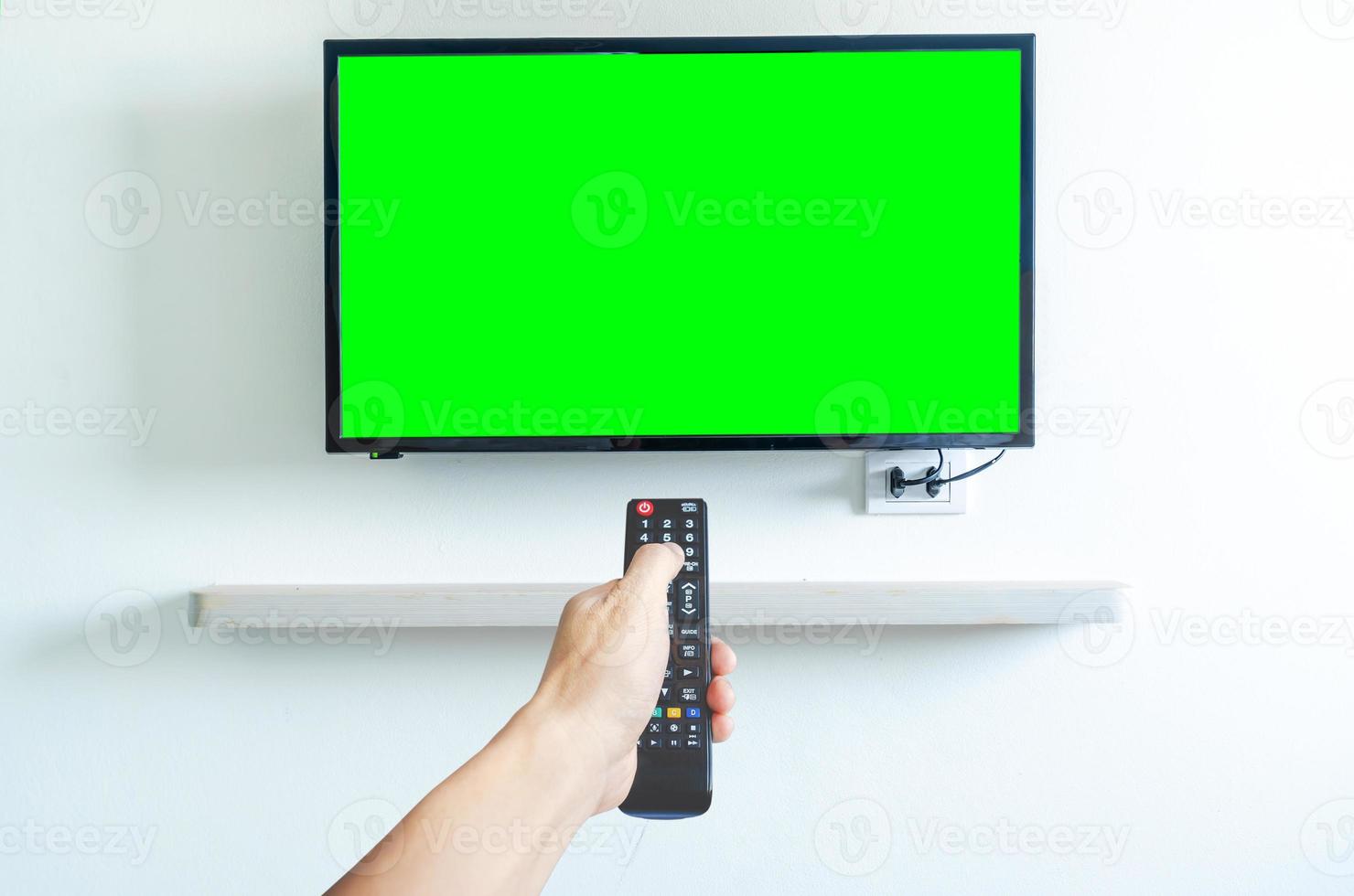 Hand holding TV remote controller over green screen a modern television set. Place for your advertisement. photo