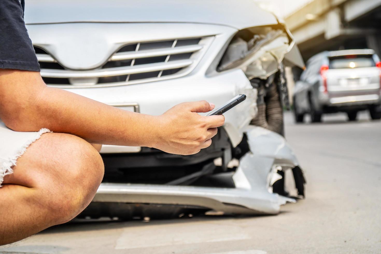 hombre que usa la ayuda de un teléfono inteligente para llamar a la compañía de seguros o al servicio de recuperación en la carretera después de un accidente de tráfico foto