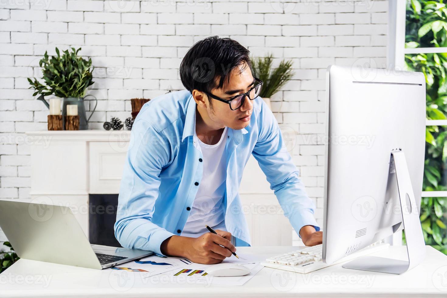 Young businessman smiling happy asian man working on a laptop and writing down ideas in a paperwork at home, work from home concept photo