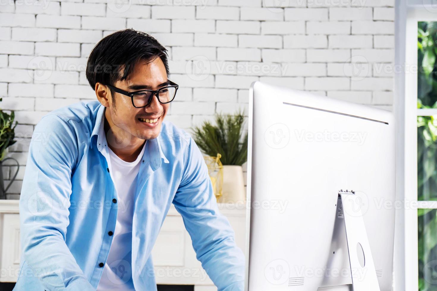Young smiling happy asian man relaxing connected on internet with laptop computer working and video conference meeting at home.Young creative typing on keyboard.work from home photo