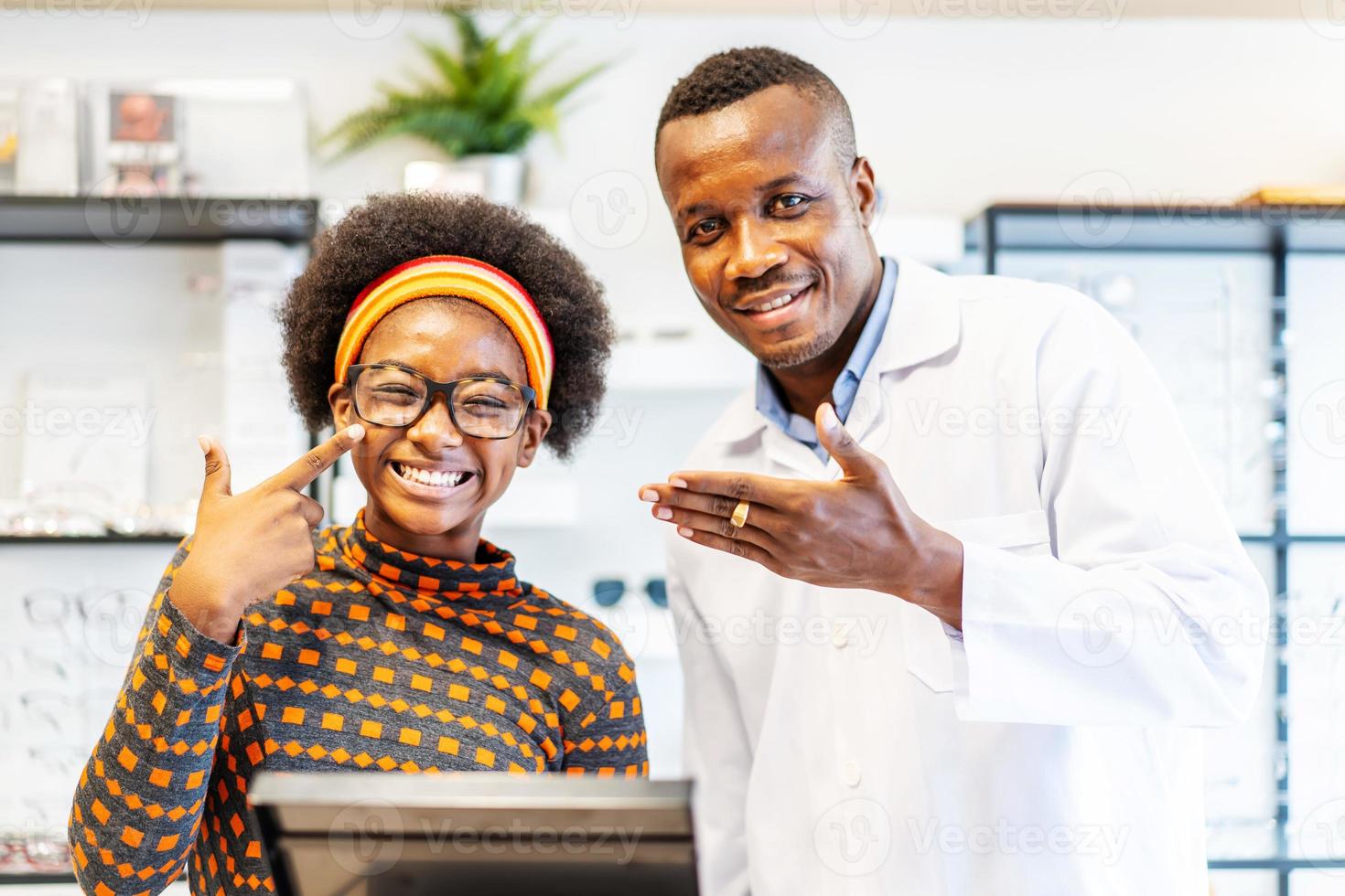 Professional ophthalmologist doctor african american man helping young woman african american client to choose a spectacles is successful. The girl is glad to have new glasses. photo