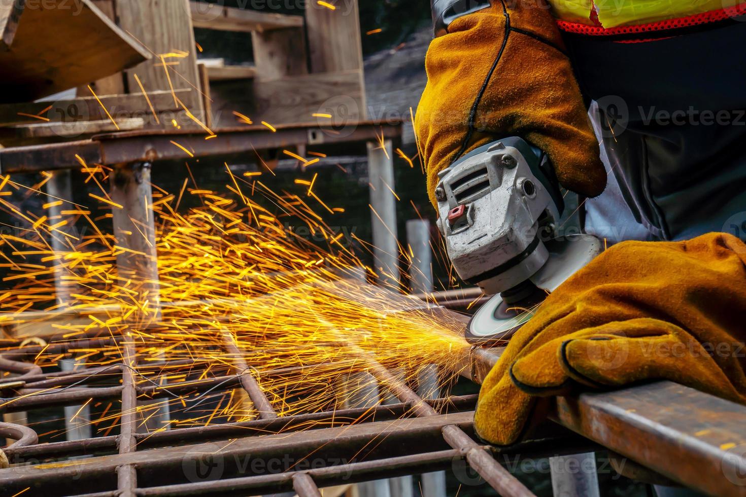 Young man welder in a working blue overall and working gloves grinds a metal object with a angle grinder in the garage, bright sparks fly to the sides photo