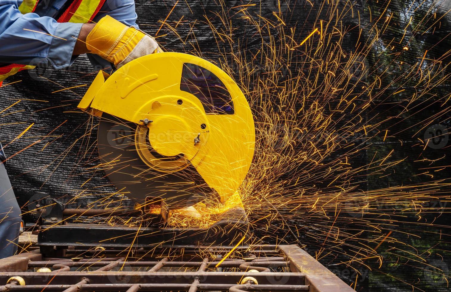 Industrial technician engineer in blue protective cloth wear safety mask, Man working with electric grinder tool on steel structure with   sparks flying in factory, selective focus photo