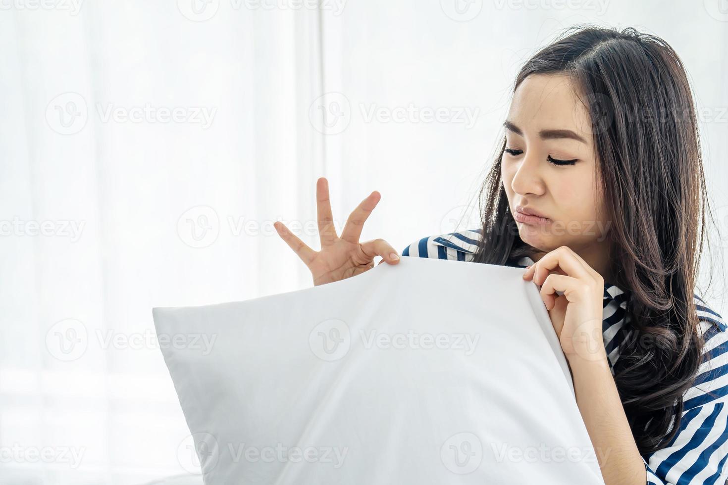Beautiful woman sniffing a white pillow with a foul odor or musty smell