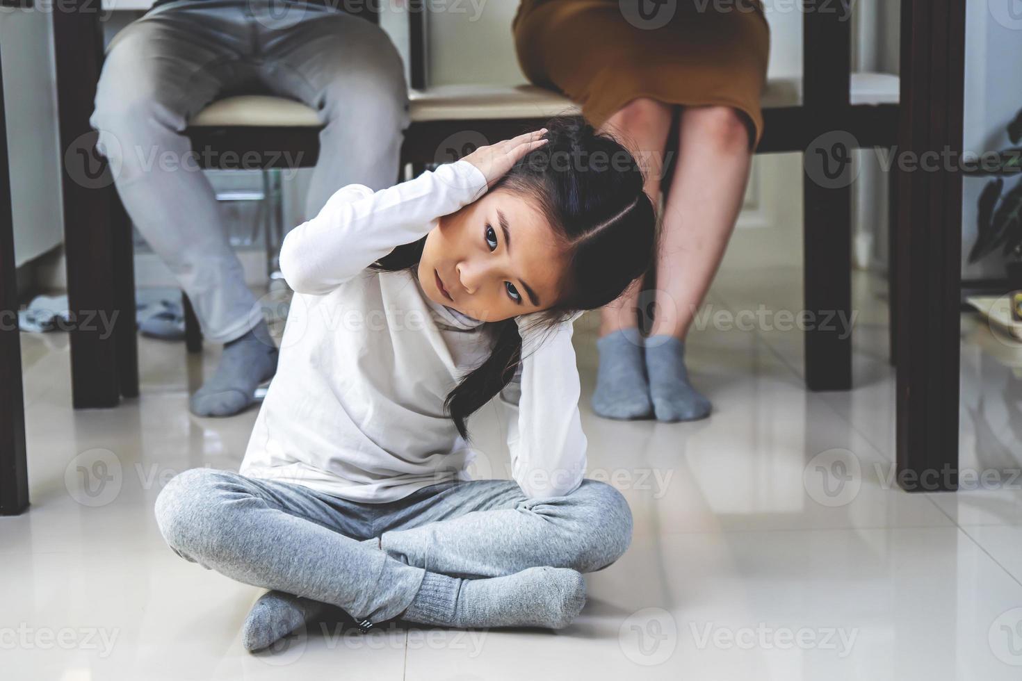 Asian little daughter sad and Clog the ears under table while parent quarrelling in kitchen, Photo design for family problems and unhappy concept