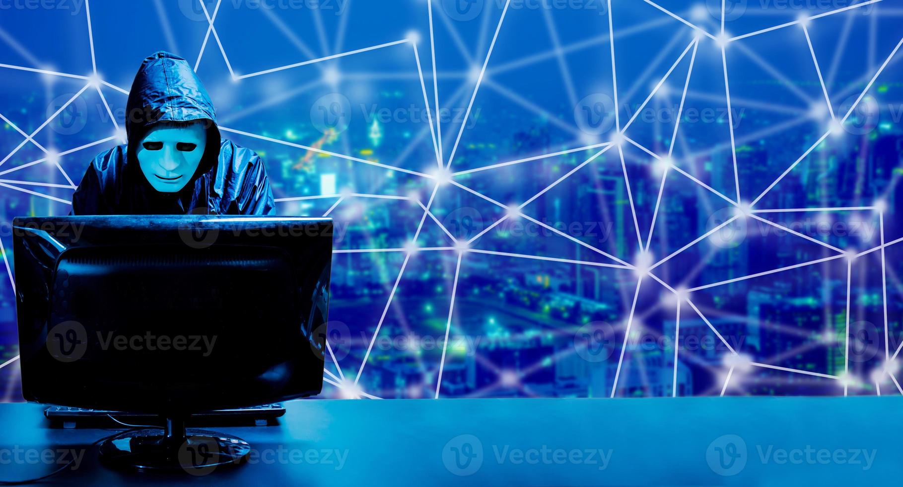 Anonymous computer hacker in white mask and hoodie. Obscured dark face standing in the middle and hacking it with his computer on  city background, Data thief, internet attack photo