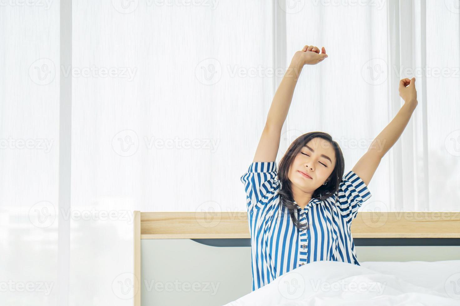 Beautiful young woman stretching in bed with her arms raised after wake up,  Healthy lifestyle, Wellness concept photo