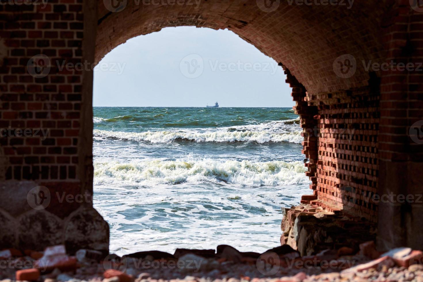 Blue sea waves seascape through red brick arch, view from old brick fort by Baltic Sea photo