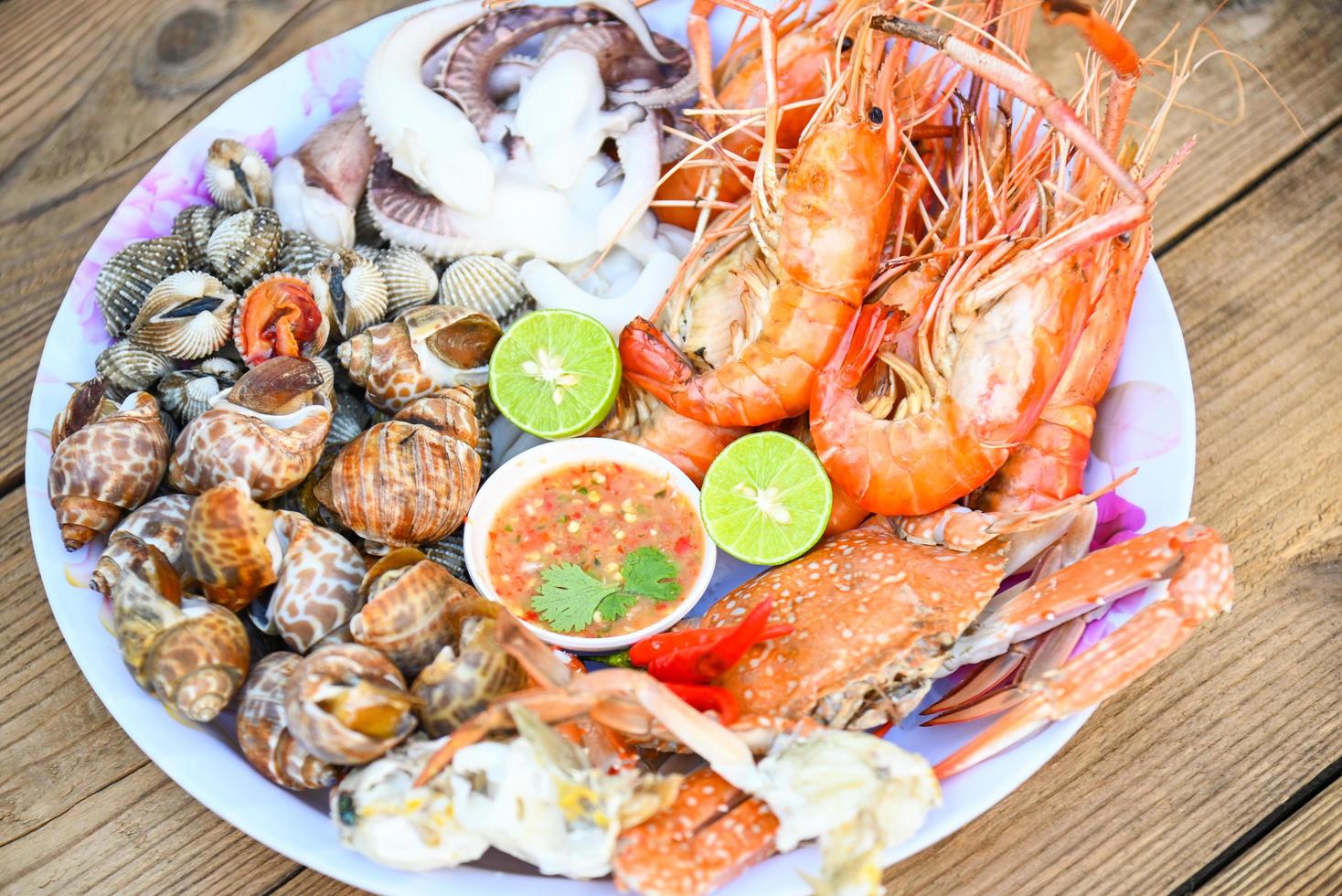 seafood plate with shrimp shellfish crab squid cockle spotted babylon with seafood sauce chili lemon lime serve on dining table, shrimps prawns seafood buffet menu cooked food photo