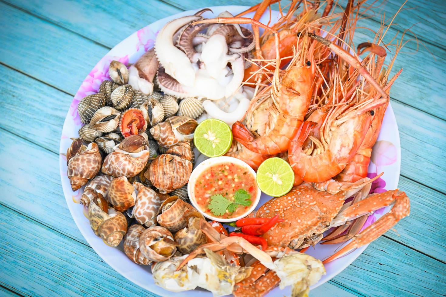 seafood plate with shrimp shellfish crab squid cockle spotted babylon with seafood sauce chili lemon lime serve on dining table, shrimps prawns seafood buffet menu cooked food photo