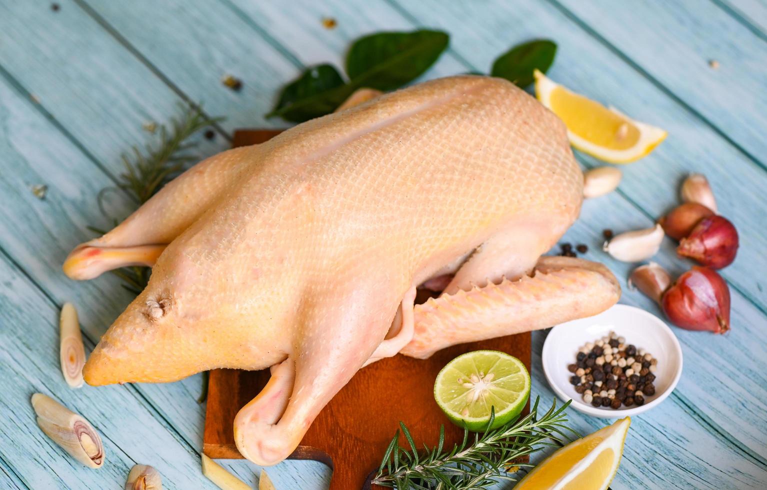 pato crudo con especias listo para cocinar en una tabla de corte de madera, carne de pato fresca en un plato para la comida, pato entero y ajo picante de limón y romero - vista superior foto