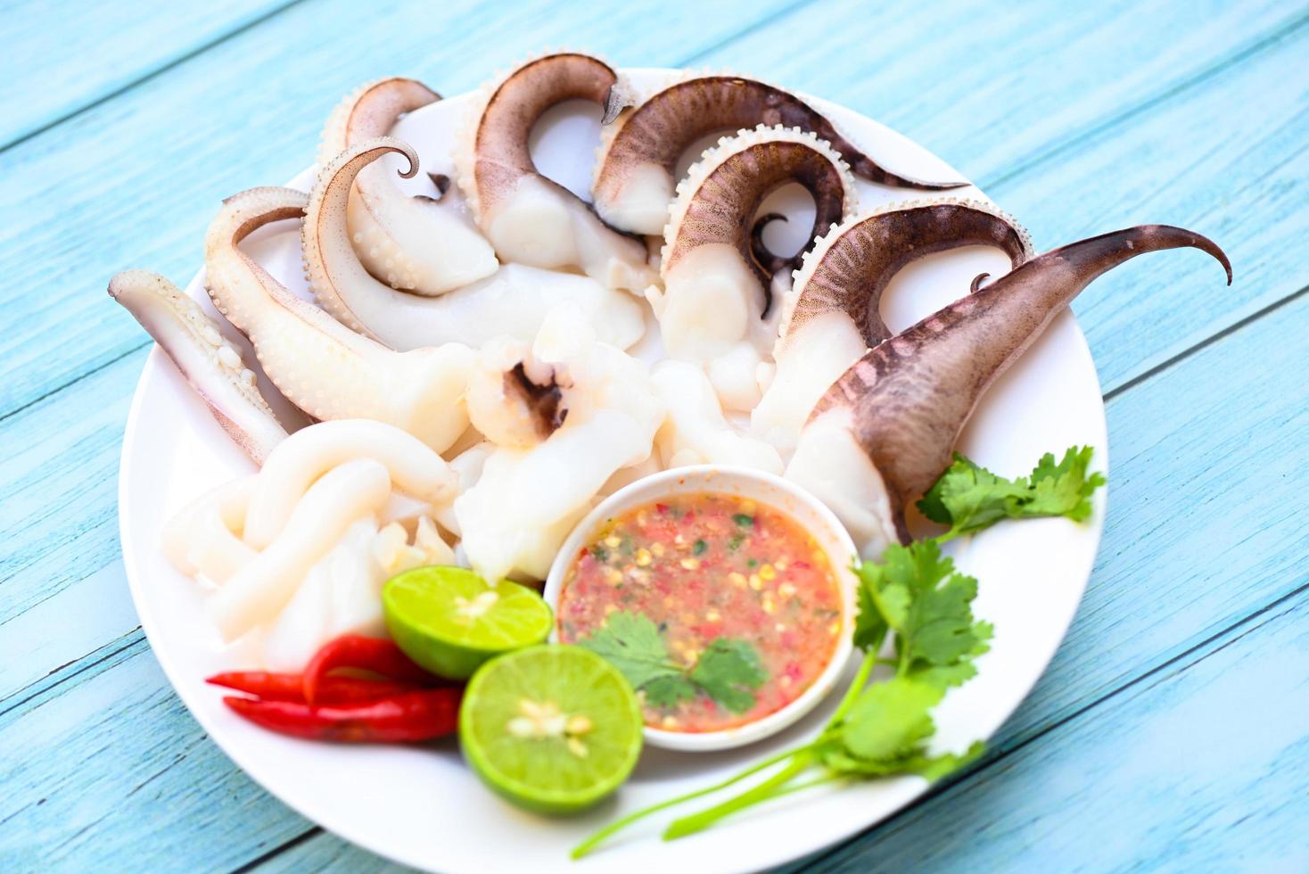 seafood plate squid food on white plate, Fresh squid cooked boiled steam with vegetable salad lemon lime and seafood sauce chili sauce serve on table, octopus tentacles cuttlefish ocean gourmet photo