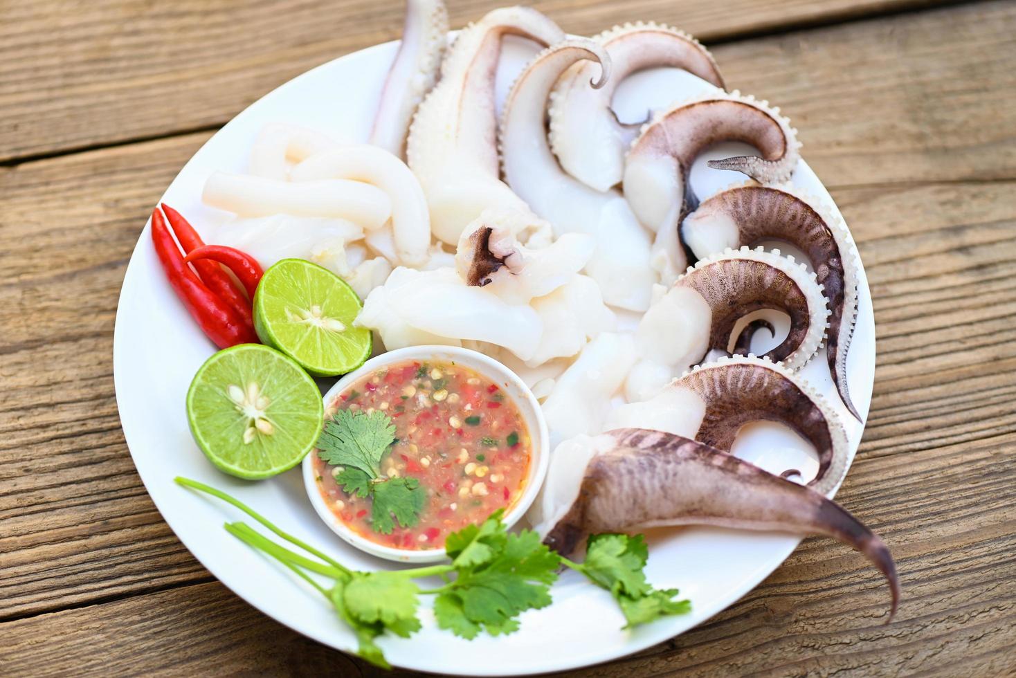 seafood plate squid food on white plate, Fresh squid cooked boiled steam with vegetable salad lemon lime and seafood sauce chili sauce serve on table, octopus tentacles cuttlefish ocean gourmet photo