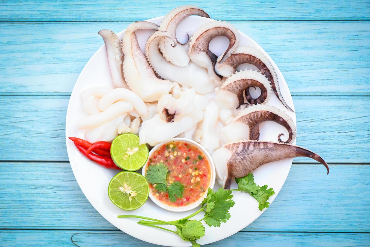 plato de mariscos comida de calamar en un plato blanco, calamar fresco cocido al vapor hervido con ensalada de verduras lima limón y salsa de mariscos salsa de chile servido en la mesa, tentáculos de pulpo sepia océano gourmet foto