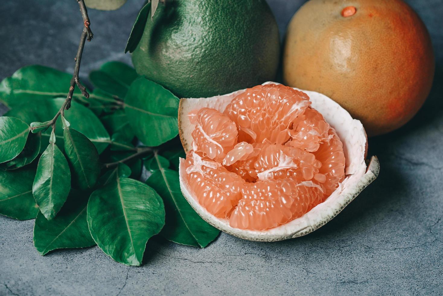 fruta de pomelo sobre fondo oscuro, pomelo fresco pelado sobre piel de pomelo y hoja verde del árbol de pomelo, pomelo, pomelo en verano fruta tropical en tailandia foto