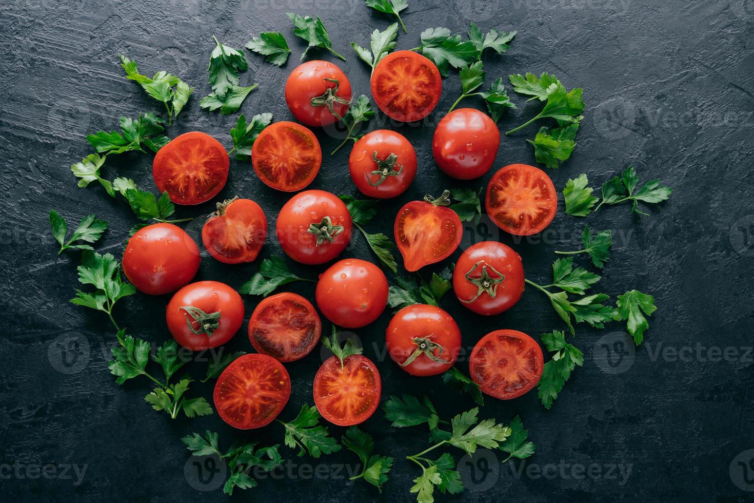 Half tomatoes and green parsley around on dark background. Fresh ingredients for making vegetarian salad. Harvested garden vegetables photo