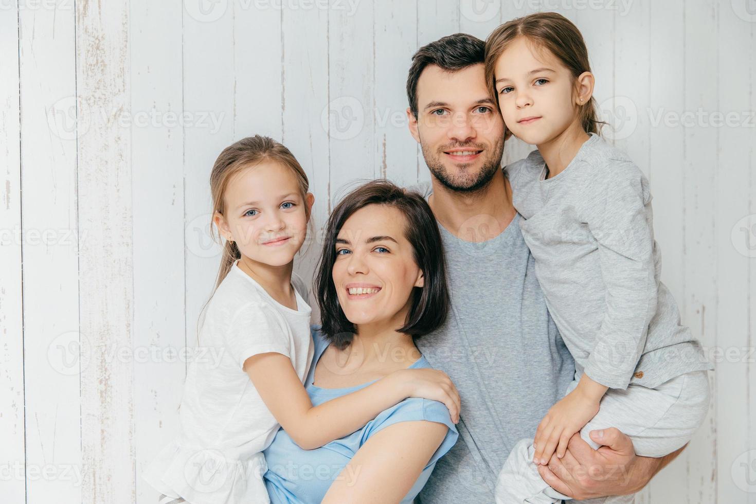 Good looking female and male parents hold their beautiful daughters, spend free time all together, enjoy togetherness. European family love each other, have fun. People, family, relations concept photo