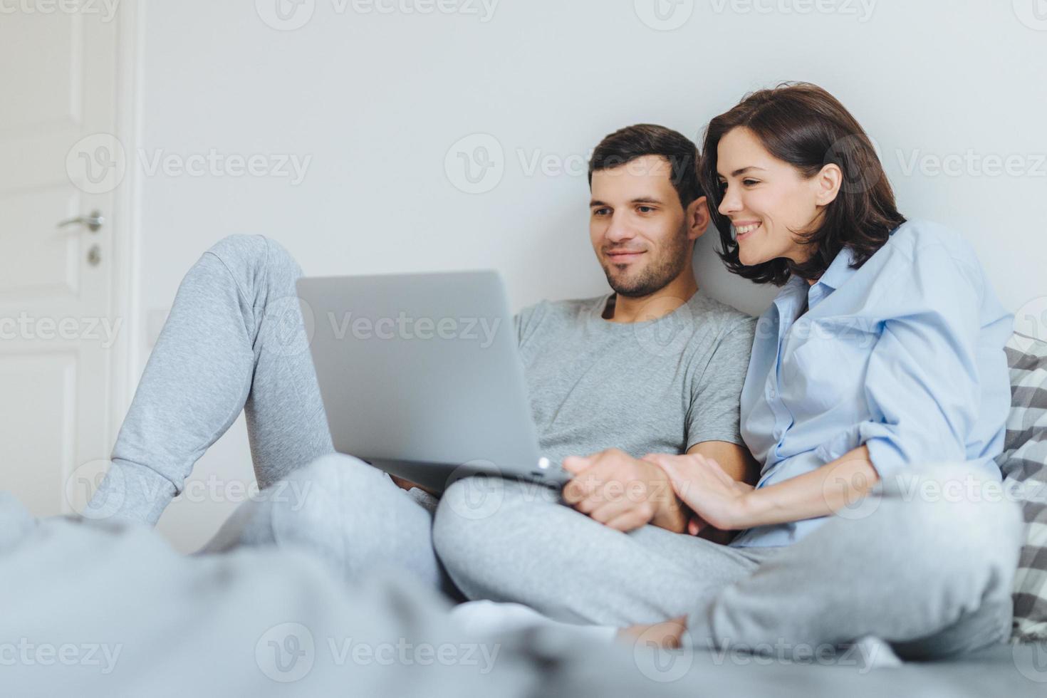 Happy couple in love review their wedding photos on laptop computer, remember plesant moments and special event in their life, use modern laptop computer and free internet connection at home