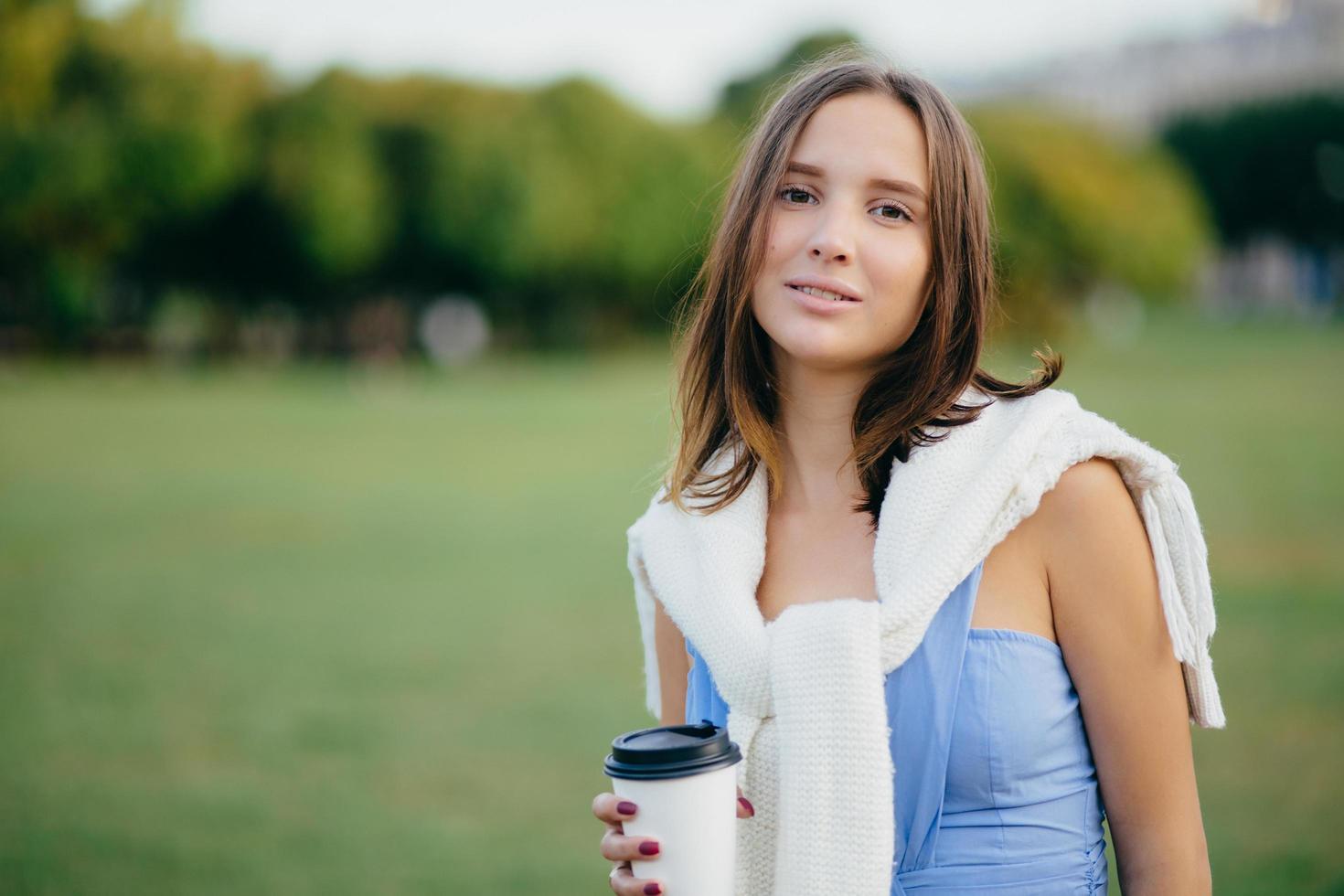 concepto de personas, recreación y estilo de vida. hermosa joven europea tiene una mirada seria a la cámara, vestida informalmente, pasa tiempo libre en la naturaleza, bebe bebidas calientes, disfruta del descanso, un ambiente tranquilo foto