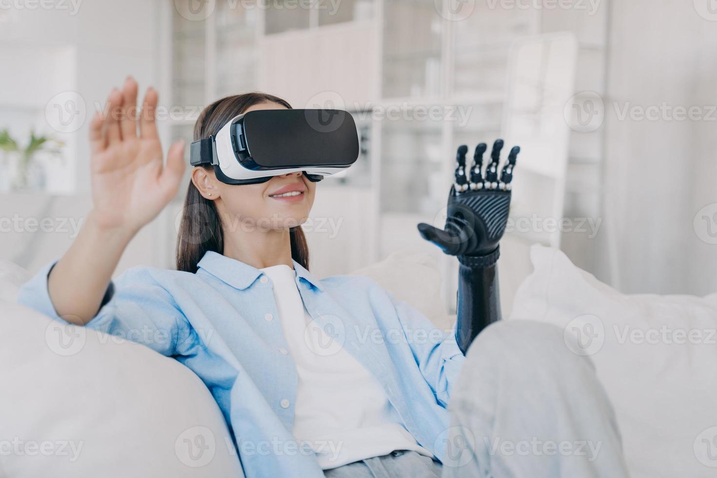 Psychological rehabilitation for handicapped. Happy girl with artificial robotic arm in vr glasses. photo