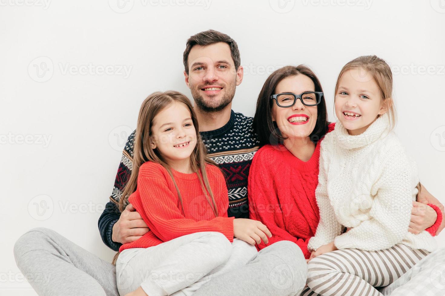 Horizontal portrait of happy male and woman embrace their small girls, have joyful expression, isolated on white background. Children and parents concept. Lovely friendly family pose indoor. photo