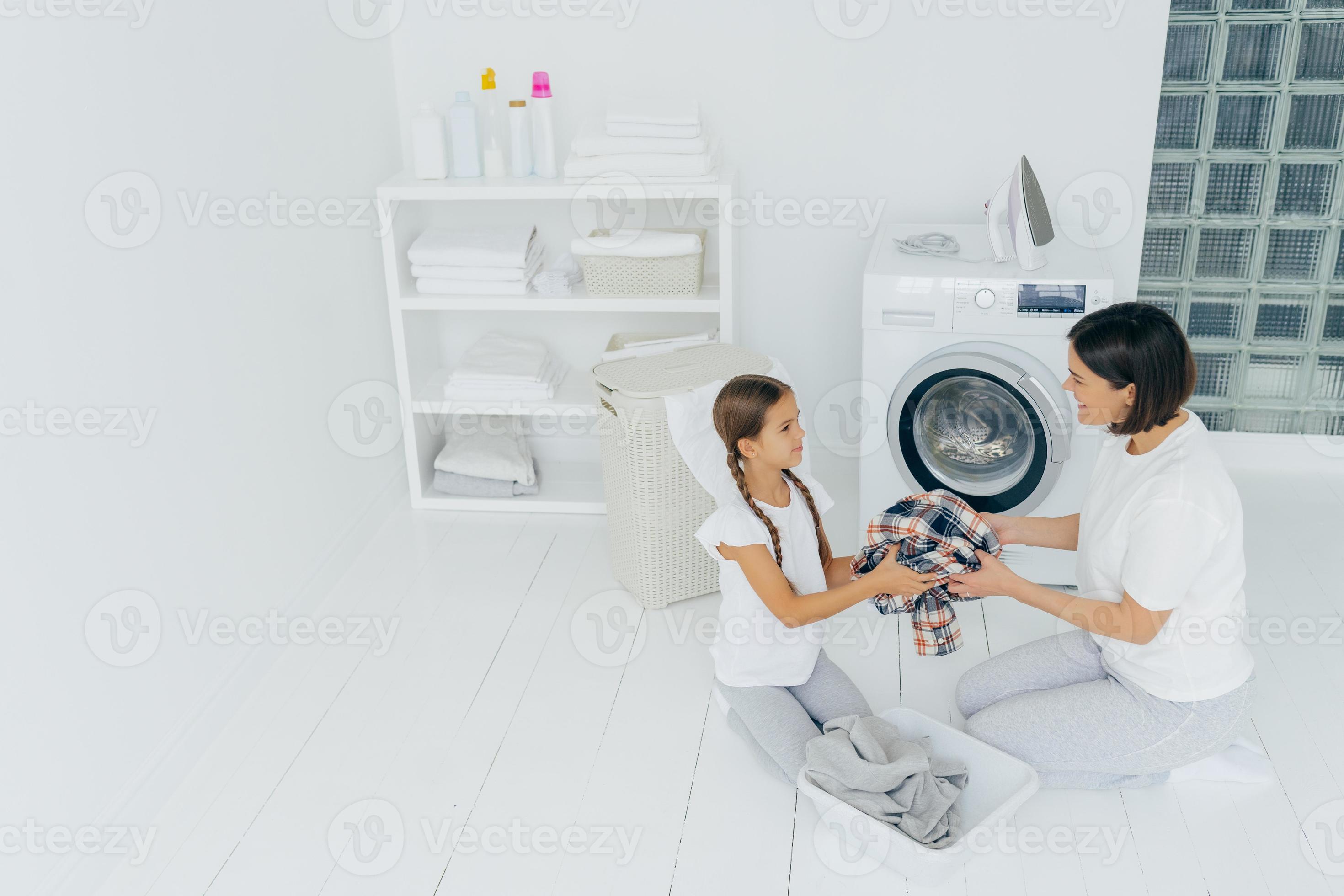 Little girl helper and her mother pose in laundry room near washing