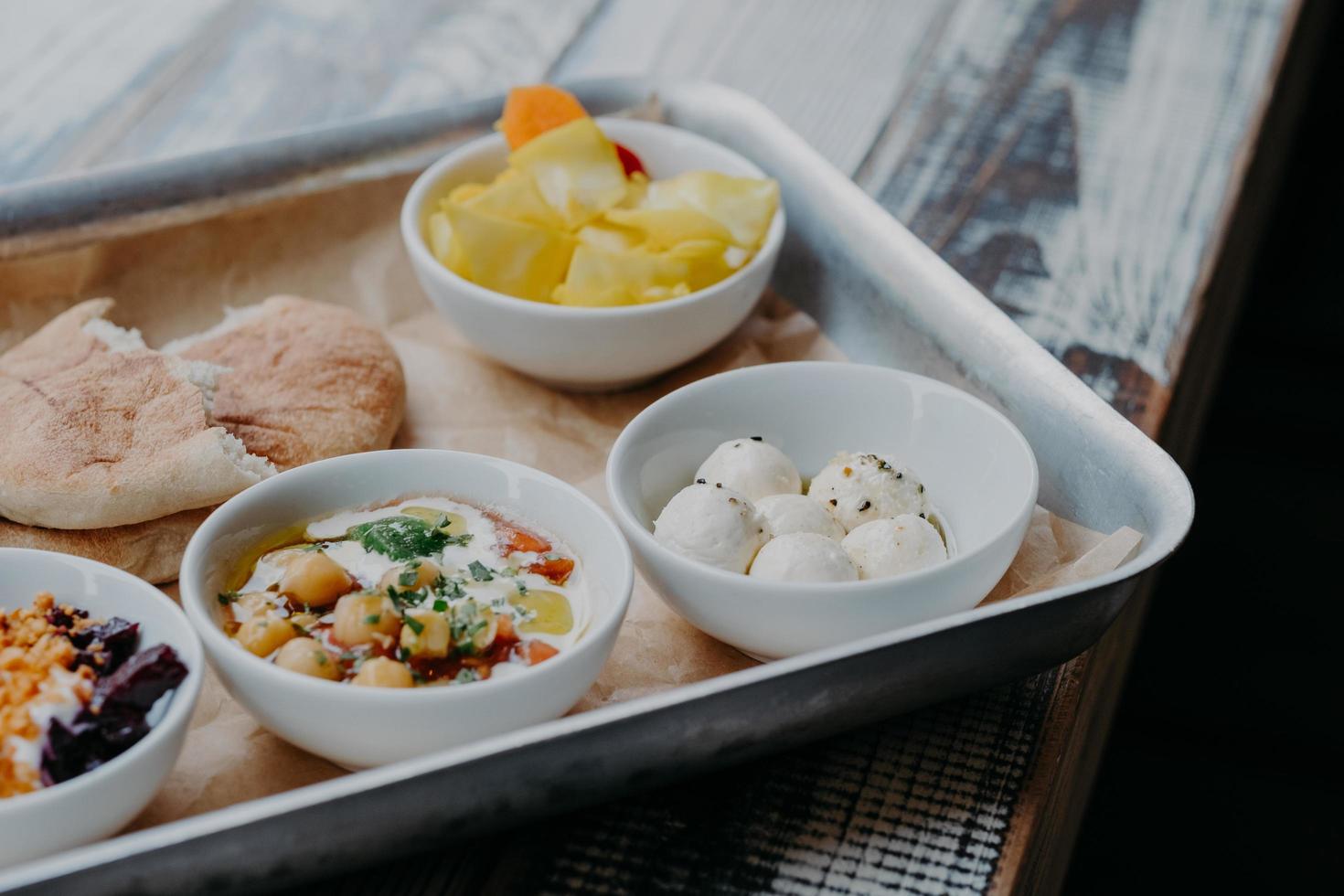 Tasty traditional dish concept. Cropped shot of tray with goat cheese, pita bread, grilled beetroot in bowls on wooden table. Israel food photo