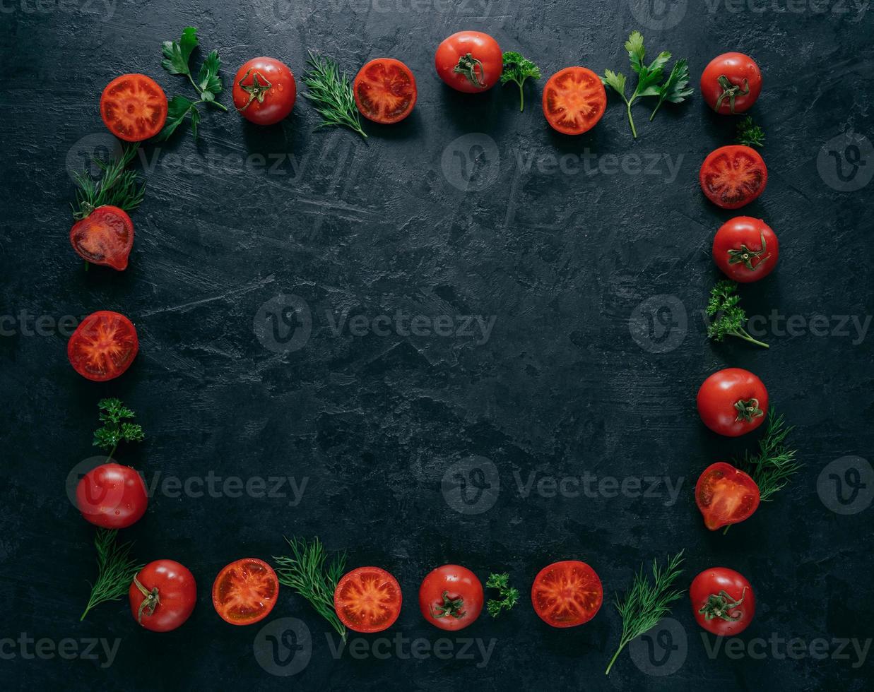 Composition of red tomatoes and green fresh parsley and dill lying on dark background in form of frame. Vegeterian food concept. Free space in middle photo