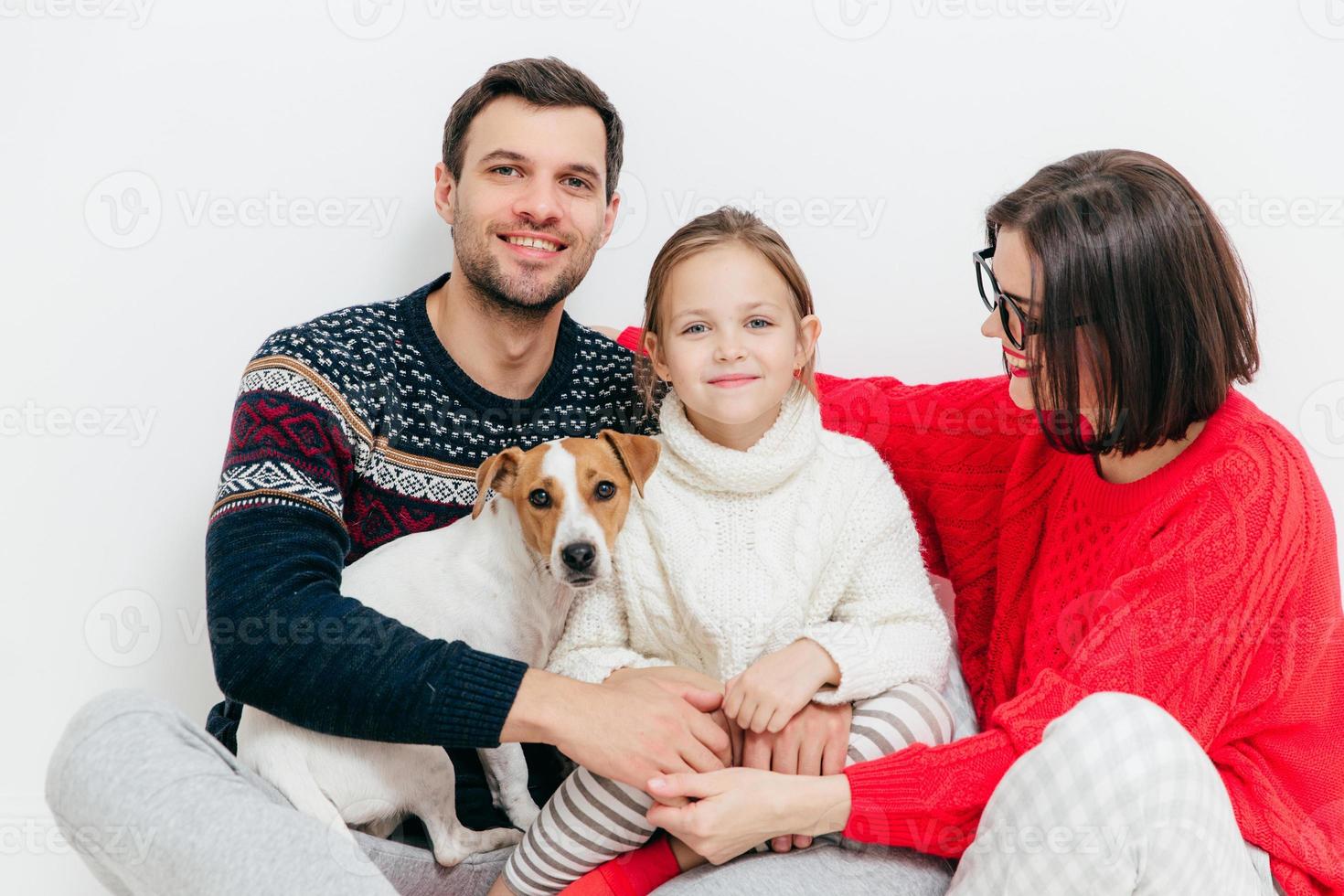 Studio shot of happy family of three family members and dog, embrace and smile happily, have good relationships, isolated on white background. Beautiful small kid with her parents and favourite pet photo