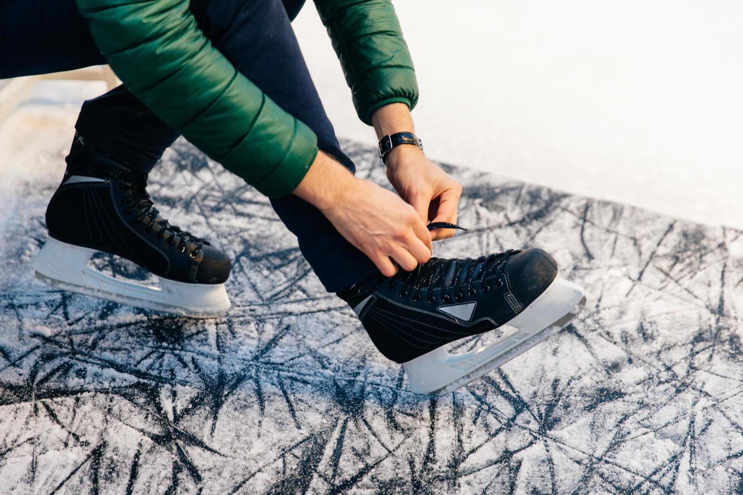 Cropped shot of unrecognizable male model being on ice covered with snow, laces up skates, going to skate with pleasure. Male advertizes new high quality skates. People and hobby concept photo