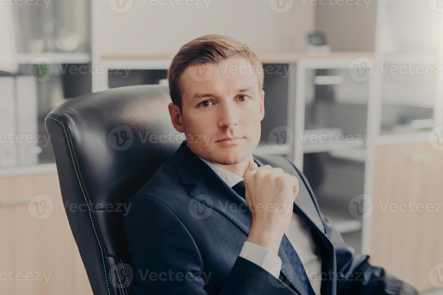 Attractive male manager sits in chair at his cabinet, dressed formally, rests for minute after hard work in office. Prosperous man boss has serious expression, works on financial report. Business photo