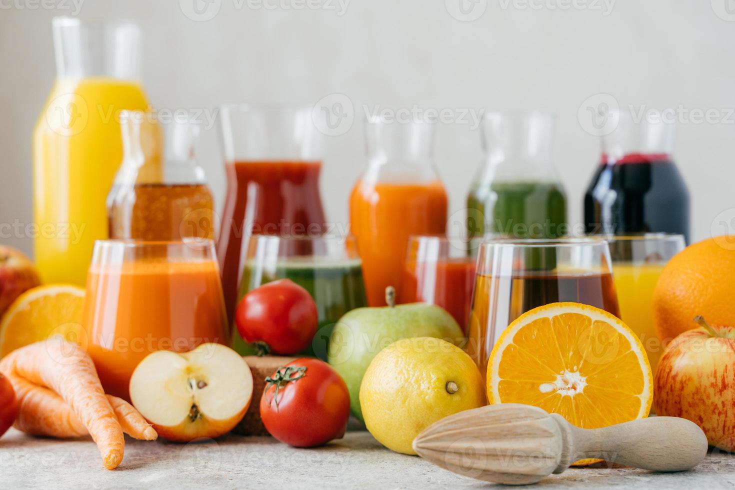 toma horizontal de frutas y verduras frescas en mesa blanca, frascos de vidrio de jugo y exprimidor de naranja. concepto de bebidas saludables. bebidas organicas foto