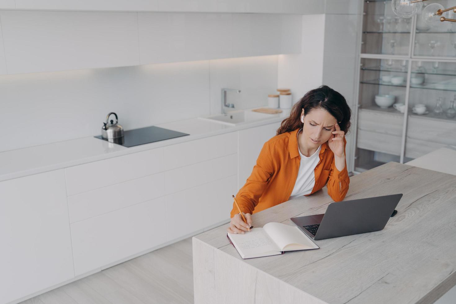 Tired spanish woman is taking notes at online conference. Teacher has remote lesson at home. photo