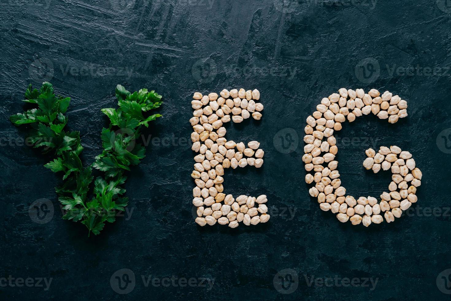 Parsley and dry garbanzo in form of letters meaning veg, vegetarian isolated over dark background. Organic protein product. Vegan food photo