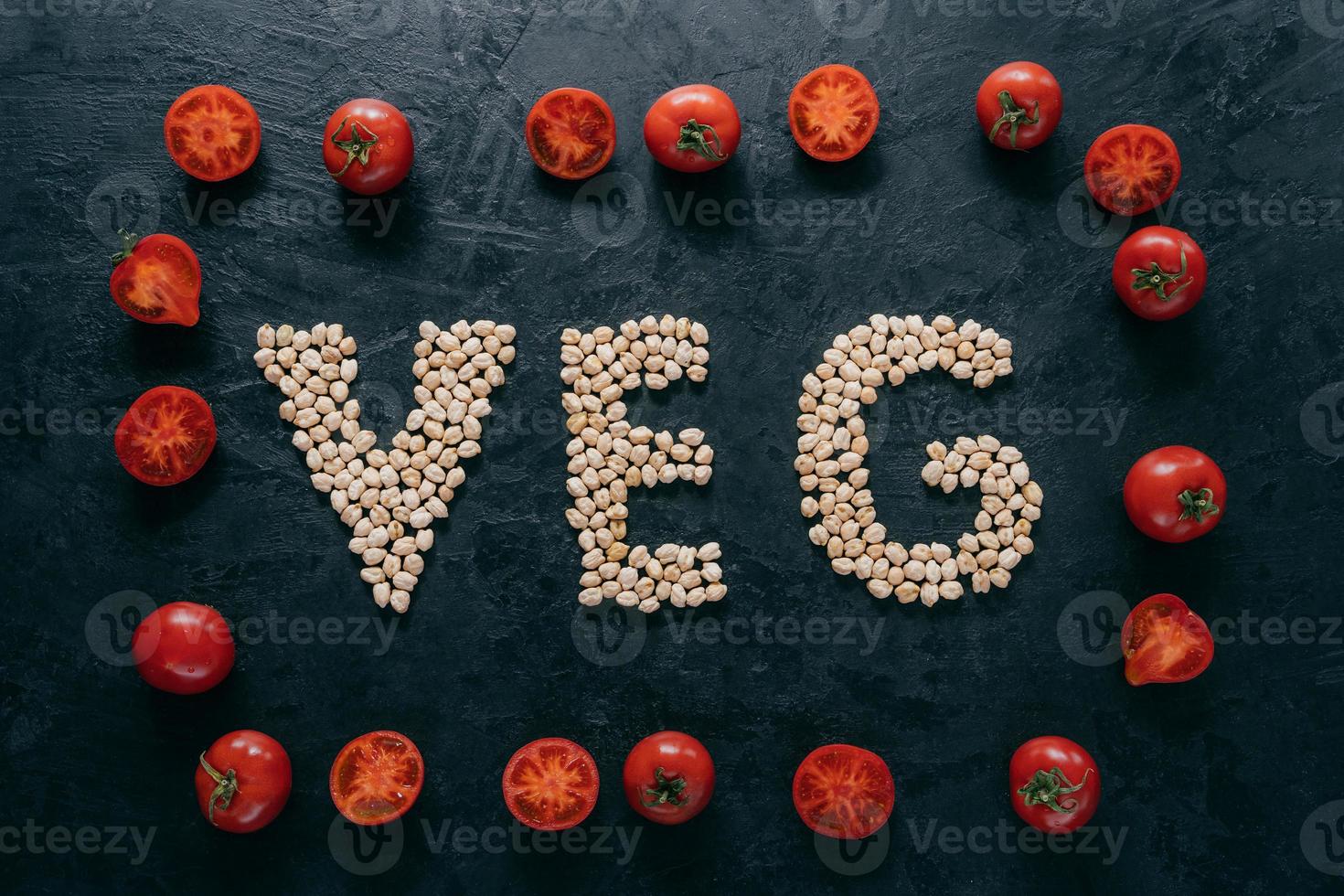 Top view of red ripe tomatoes in form of frame and letter shaped chickpeas on dark background. Vegan food concept. Organic nut. Vitamin photo