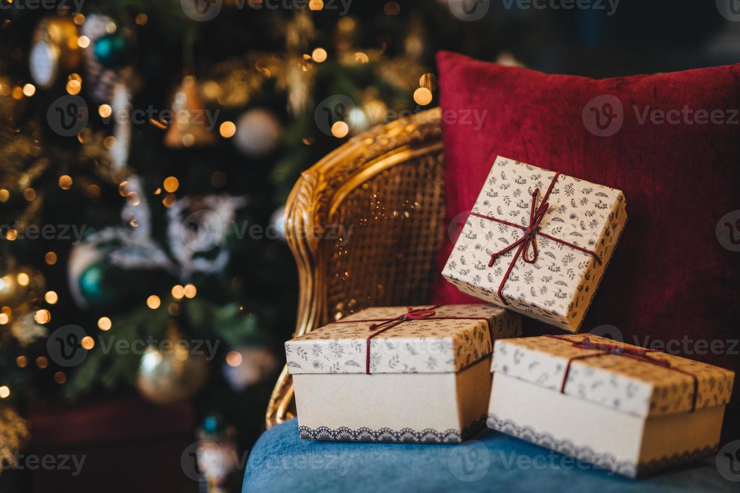 Picture of wrapped gift boxes lie on armchair against decorated New Year tree background. Preperation for holiday. Beautiful Christmas tree with garlands and presents indoors photo