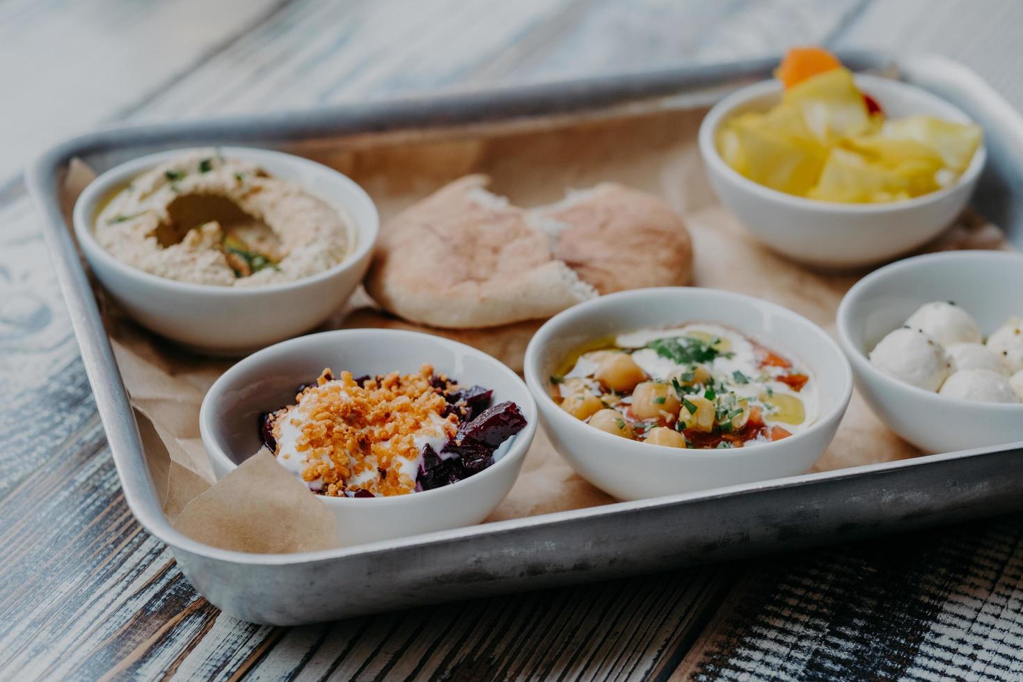 Food and nutrition concept. Traditional Israel dish for dinner. Tray of delicious hummus, beet with spices, core of tomatoes, pita bread, goat cheese served for you photo