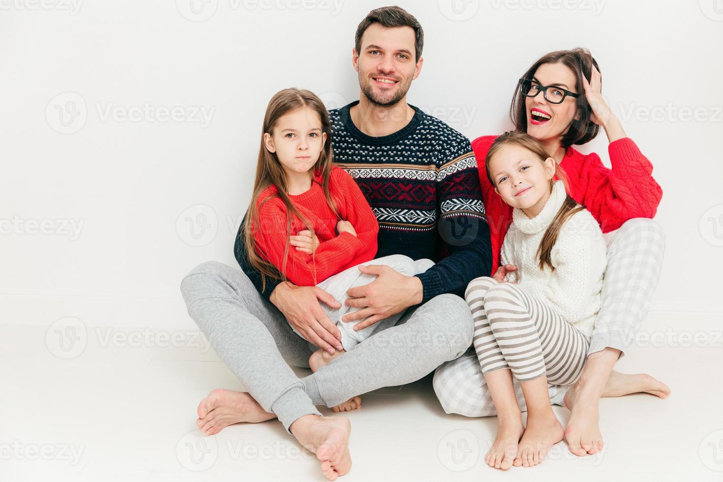 retrato de familia feliz de cuatro miembros mujer morena atractiva, su marido y dos hijas pequeñas se sientan en el suelo, aislado sobre fondo blanco. concepto de paternidad. encantadora familia interior. foto