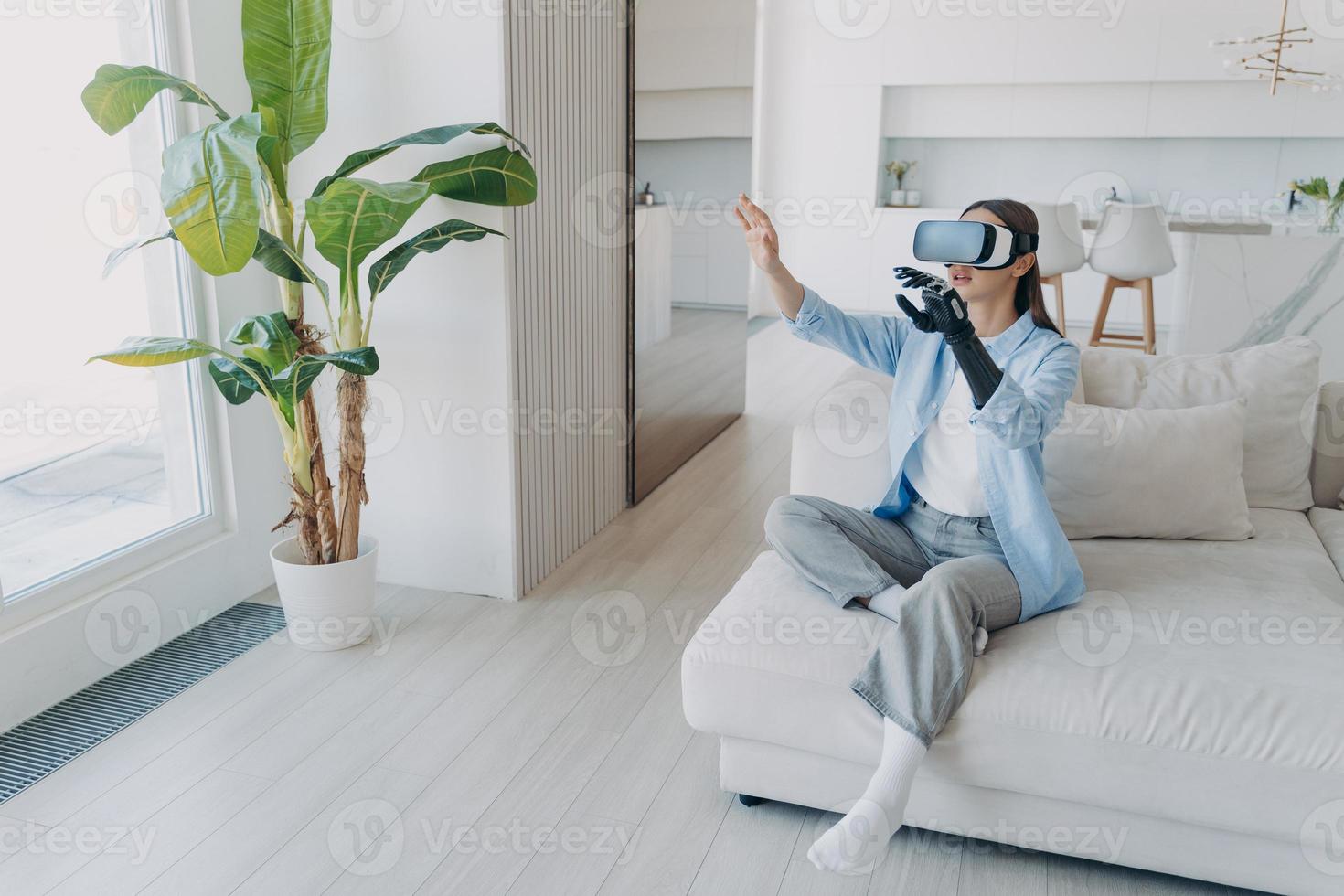 Handicapped girl with cyber arm in vr glasses at home. Technology for recovery and rehabilitation. photo