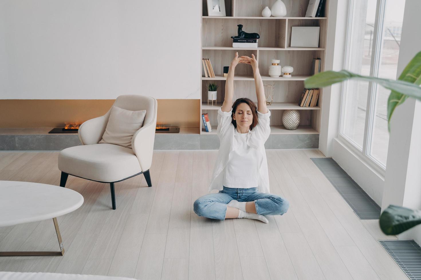 Girl is doing stretching exercises on floor at home. Happy woman is meditating with her eyes closed. photo